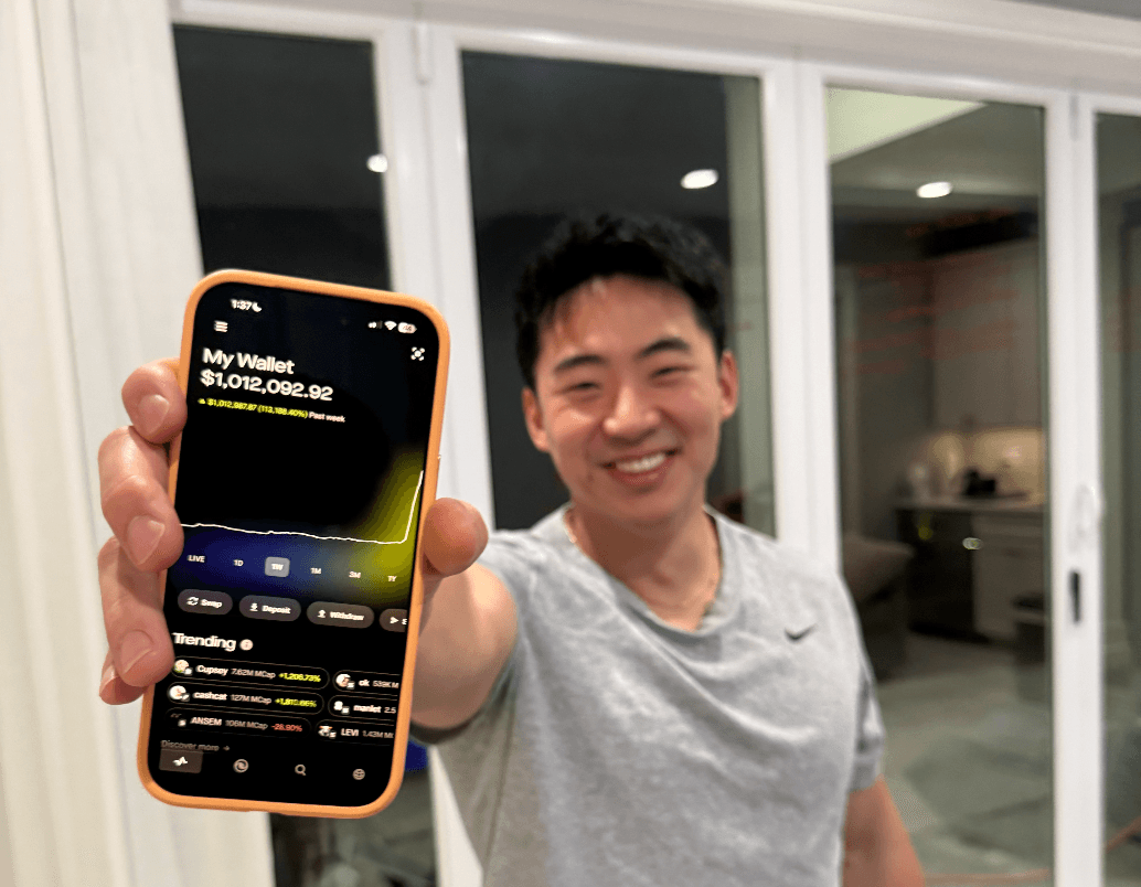 Brian holding a phone showing a $1,012,092.92 wallet balance.